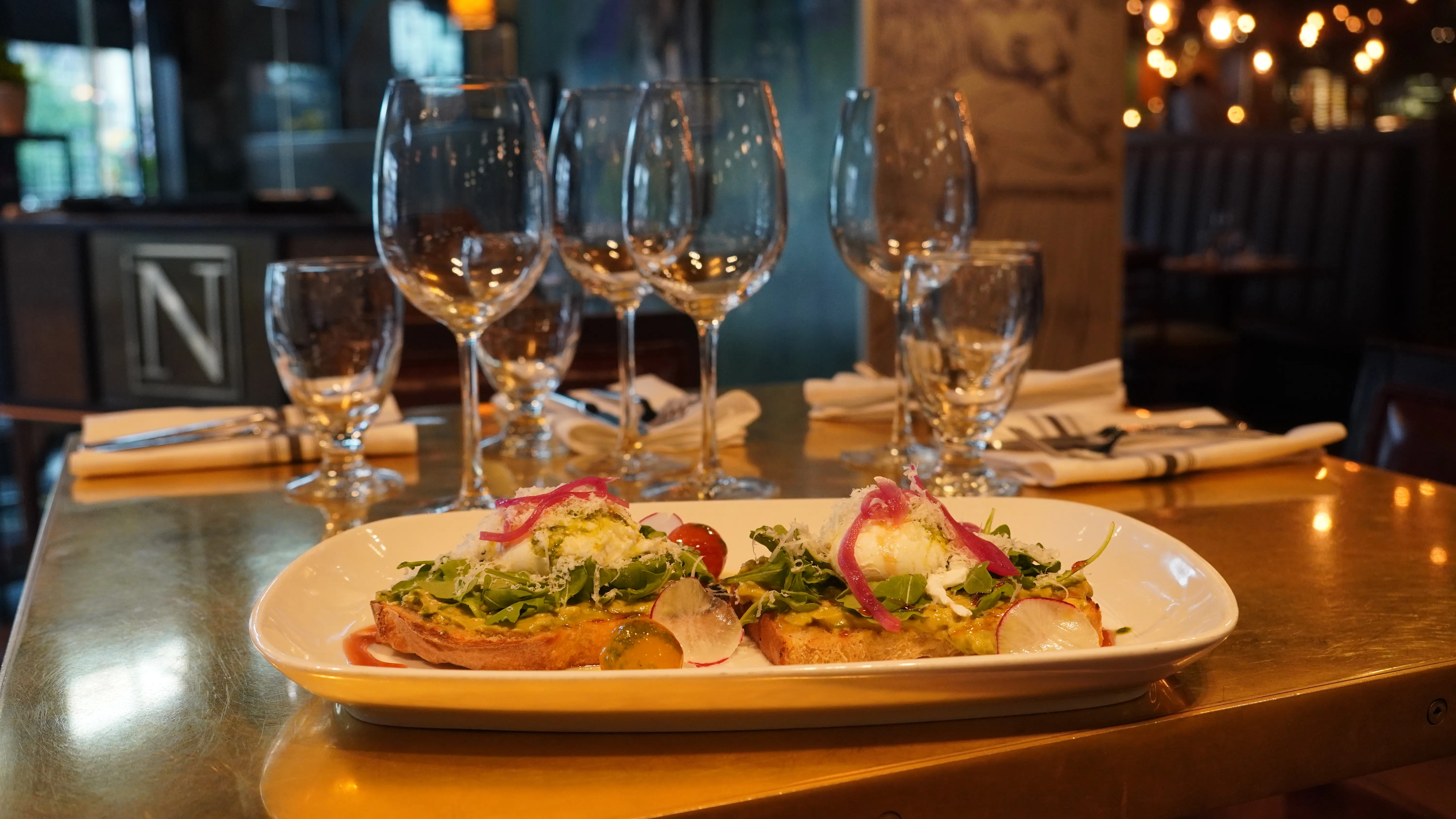 Shared crostini topped with greens, radish and pickled red onion on a brass table at notable - The Steakhouse, northwest Calgary